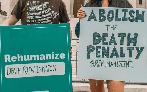 Two people hold signs about rehumanizing death row inmates and abolishing the death penalty (Unsplash/Maria Oswalt)