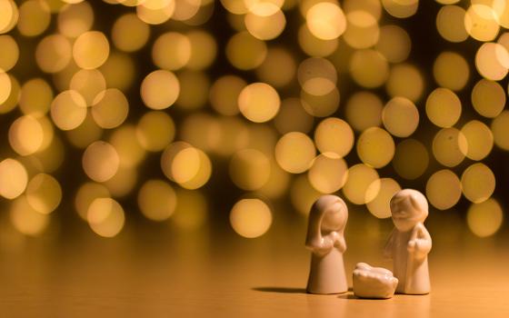 Figurines of Mary, Joseph and baby Jesus are pictured against several shining lights in this photo illustration. (Unsplash/Gareth Harper)