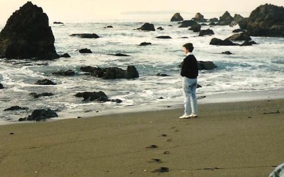 Woman stands at the edge of water on beach.