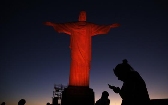 People are pictured in a file photo standing in front of the statue of Christ the Redeemer in Rio de Janeiro as it is lit up in orange to commemorate the Day against Human Trafficking and Missing Persons observed by the Archdiocese of Rio de Janeiro. (OSV News/Reuters/Pilar Olivares)