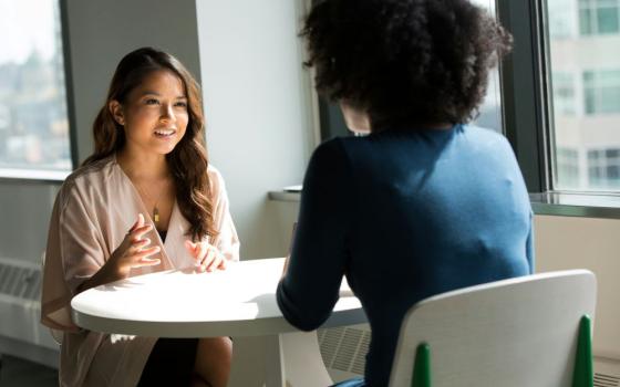 Two women sit across from each other at small table.