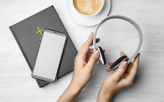 A woman's hands hold headphones next to a Bible with a smartphone on top and a cup of coffee (Dreamstime/Chernetskaya)