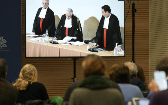 Reporters watch a screen in the Vatican press room showing Vatican tribunal president Giuseppe Pignatone reading the verdict of a trial against Cardinal Angelo Becciu and nine other defendants. 