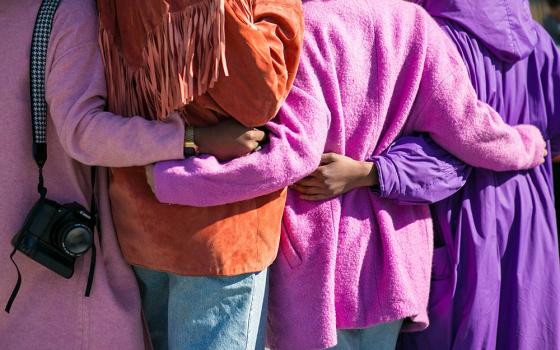 Women stand arm in arm outside (Unsplash/Vonecia Carswell)