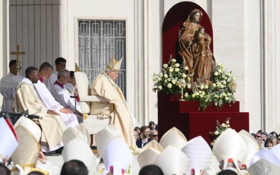 Pope Francis, vested, sits during Mass before statue. 