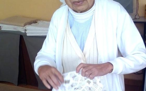 The sister stands at a table, handling textiles. 