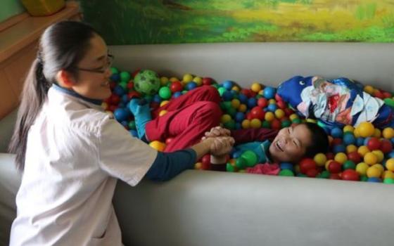 Sr. Magdalena works with a child in a tub filled with plastic balls,