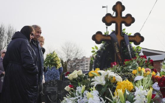 People gather outdoors around cross bedecked with flowers