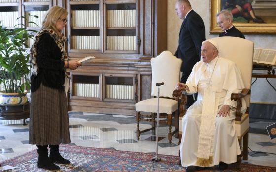 Pope Francis, seated, smiles while listening to Maeve Heaney speak.