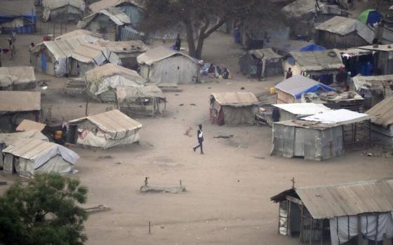 Person walks through large, dusty square enclosed by shanties. 