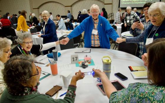 Women stand around table and hold hands. 