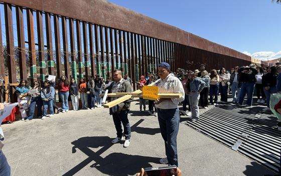 A participant in a symbolic Via Crucis held Saturday in Nogales, Mexico, to honor migrants uses a smartphone (at bottom) to take a picture of the group that includes a man holding a wooden cross next to the border wall with Arizona. The orange sign reads,"We are the body of Christ." (Anita Snow)