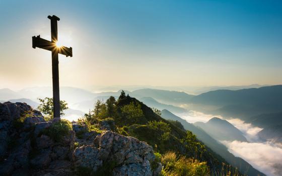 Cross lit by sunlight atop a mountain range (Unsplash/Theo Crazzolara)