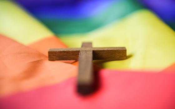A wooden cross lies on a rainbow flag in this 2021 file photo. In an email to community members at the News Orleans Archdiocese school from which he was dismissed, Mark Richards said that he was fired because a parent notified officials about an obituary for his husband, who died in September 2023. (OSV News/KNA/Julia Steinbrecht)