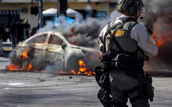 Smoke rises from a burning car on Atlantic Boulevard during a standoff by protesters and law enforcement, following multiple detentions by U.S. Immigration and Customs Enforcement in Compton, California, on June 7, 2025. (OSV News/Reuters/Barbara Davidson)