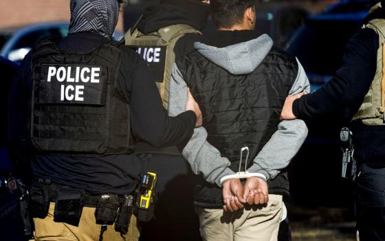 Man with Police ICE vest escorts handcuffed man.