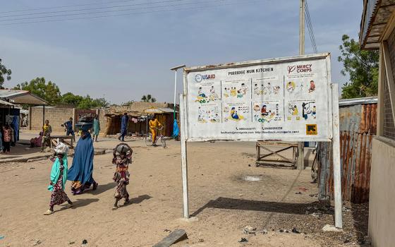 A woman and her children walk past a sign for a U.S. Agency for International Development program in Dikwa, Nigeria, April 29, 2025. (AP/Sunday Alamba)
