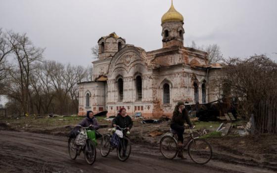 Residents walk with their bicycles in front of a damaged church, in Lukashivka, in northern Ukraine  April 22, 2022.(RNS/AP/Petros Giannakouris)