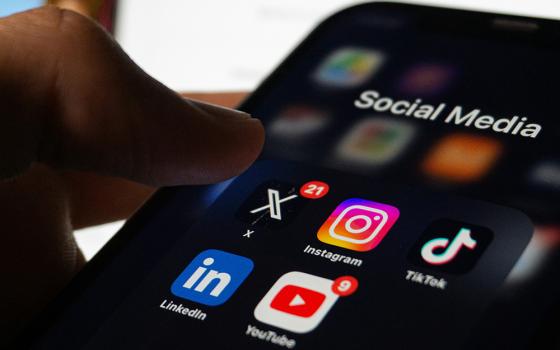 A close-up photo illustration shows a user hovering with their thumb over social media app icons displayed on a smartphone. (Unsplash/Berke Citak)