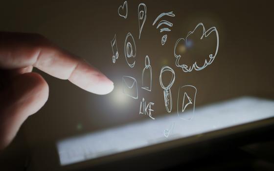 A photo illustration show a hand hovering over a smart device, with drawings of social media buttons and tags floating above the screen. (Pixabay/Edar)