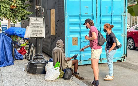Volunteers offer information and a Metro card to a homeless man outside of the Martin Luther King Jr. Library in Washington, D.C. (NCR photo/James V. Grimaldi)