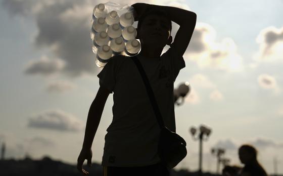 A young street vendor carries plastic bottles of water on his shoulder on a summer day, in Istanbul Aug. 8, 2025. (AP/Francisco Seco)