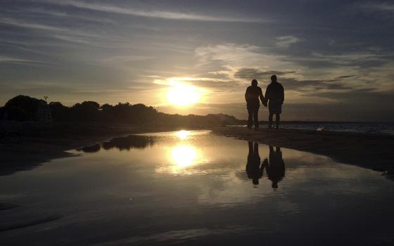 A couple is pictured in a file photo walking along Gillson Beach holding hands as the sun sets in Wilmette, Illinois. "Sometimes I come close to tears, not out of weakness, but from the exhaustion of seeing truth and kindness diminish in public life," writes NCR editor/publisher emeritus Thomas Fox. (OSV News/Reuters/Jim Young)