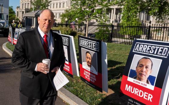 White House border czar Tom Homan walks to do a television interview at the White House April 28 in Washington. The signs show photos of people the Trump administration says are undocumented immigrants who have been arrested.