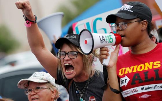Woman wears T-shirt that says "Unions" and speaks into megaphone.