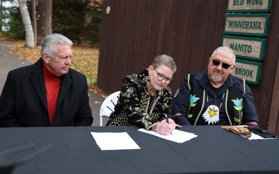 Lac du Flambeau Business Development Corporation CEO Larry Turner (left) and Lac du Flambeau Band of Lake Superior Chippewa Indians President John Johnson Sr. (right) look on as Sr. Sue Ernster  signs title documents for property the Franciscan Sisters of Perpetual Adoration had owned Oct. 31. The nearly 2-acre parcel is about 15 minutes east of the Lac de Flambeau Reservation. (Courtesy of the Franciscan Sisters of Perpetual Adoration)