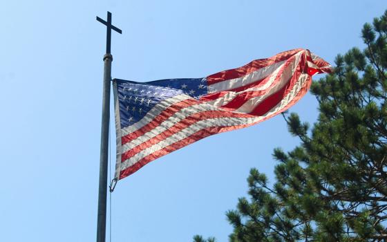 Cross on top of flagpole with United States flag flying (Unsplash/Cody Otto)