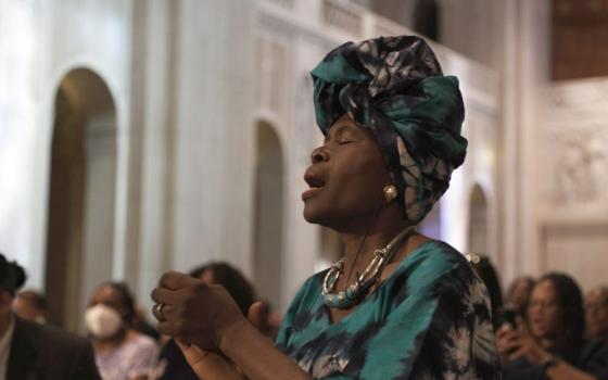 A Black woman sings or prays in still image from new film.