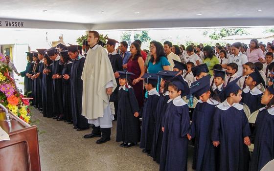 Then-Fr. Ronald Hicks prays with students from Nuestros Pequeños Hermanos in Texistepeque, El Salvador in this photo from a graduation in 2005. Hicks spent five years, 2005-2010, working with the organization for abandoned and vulnerable children. (Courtesy of Nuestros Pequeños Hermanos)