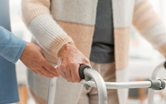 A person uses a walker with a health care worker assisting (Dreamstime/Yuri  Arcurs)
