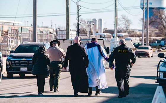 Scalabrinian Fr. Leandro Fossá, pastor of Our Lady of Mount Carmel Parish (right); Clarentian Fr. Paul Keller, missionary priest and provincial leader (center); and Sr. Alicia Gutierrez, a member of the congregation of the Society of Helpers (left) walk toward the ICE Broadview detention center escorted by two officers on Feb. 18, 2026. (Courtesy of Coalition for Spiritual and Public Leadership/Derek Carter)