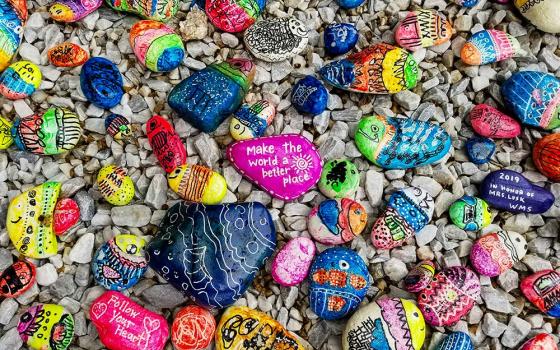 Painted stones with colorful fish and the messages "Make the world a better place" and "Follow your heart" (Unsplash/Simon Ray)
