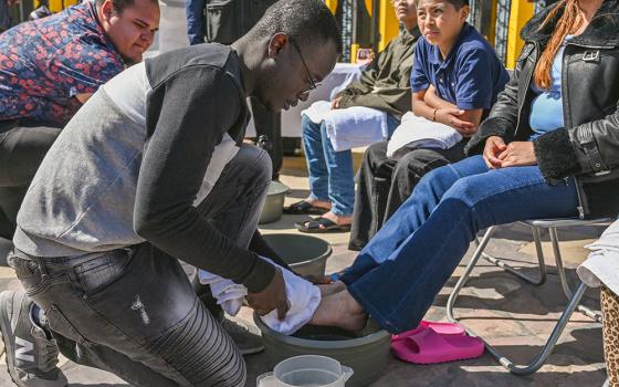 Haitian migrant and volunteer Djephy Wood Denios from La Casa del Migrante in Tijuana, Mexico, cleans the feet of a woman during the annual washing of the feet ceremony on Holy Thursday at Tijuana's Friendship Park circle on the U.S.-Mexico border April 17, 2025. (OSV News/Carlos A. Moreno)