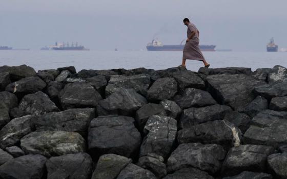 A man walks along the shore as oil tankers and cargo ships line up in the Strait of Hormuz, as seen from Khor Fakkan, United Arab Emirates, March 11, 2026. (RNS/AP/Altaf Qadri)