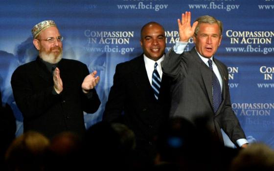 Rabbi Mark Borovitz, from left, and Julio Medina look on as President George W. Bush takes the stage to make remarks at the first meeting of the White House National Conference on Faith-Based and Community Initiatives, June 1, 2004, in Washington. (RNS/AP/Lawrence Jackson)