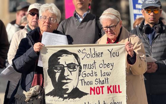 Religious of the Sacred Heart Sr. Diane Roche, left, helps hold a banner with the image and words of St. Oscar Romero, as she prays March 24, 2026 in front of the headquarters of U.S. Immigration and Customs Enforcement. She celebrated Romero's feast day by demanding that the agency put a stop to the violent tactics of some of its agents. (GSR photo/Rhina Guidos)