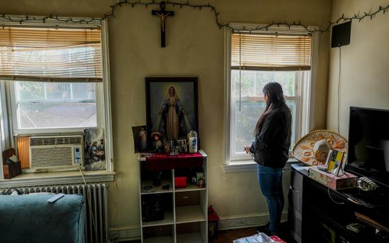 A parishioner of the Shrine of the Sacred Heart whose husband was detained by immigration agents looks out her home's window in Washington, D.C., Oct. 10, 2025. (AP/Luis Andres Henao)