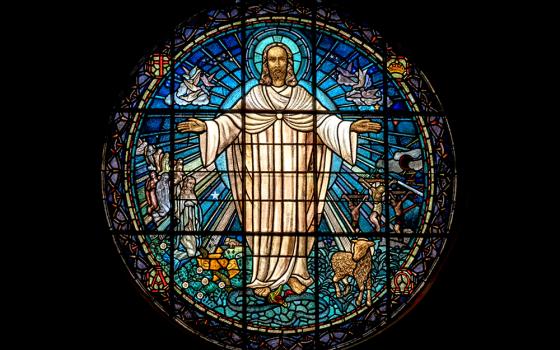 Jesus is rendered in a stained-glass window that shines bright in a dark room. (Unsplash/Paul Zoetemeijer)