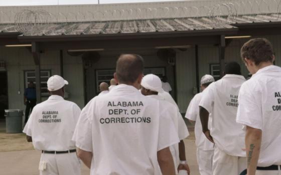 A still image shows a scene from "The Alabama Solution," nominated for a Best Documentary Feature Oscar, shows a group of men in white shirts that say, "Alabama Dept of Corrections" 