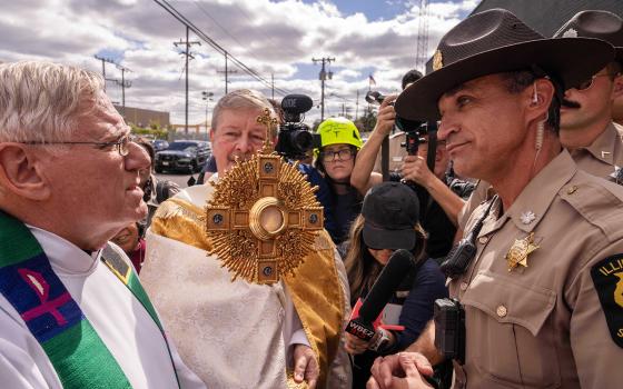 A member of the Illinois State Police, right, relays the message to clergy that U.S. Immigration and Customs Enforcement denied them access to detainees to provide Communion, outside an ICE facility in Broadview, Ill., Oct. 11, 2025. (RNS/AP/Adam Gray)