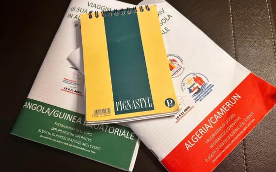 The notebook used by NCR Vatican correspondent Justin McLellan during his trip through Africa with the pope laid on top of two programs.