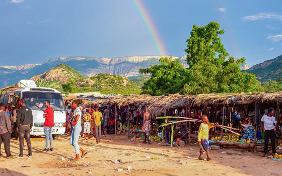 A rainbow hangs above mountains in the distance as people shop at a food market in Lubango, Angola, March 21, 2025. (Dreamstime/Joyfull)