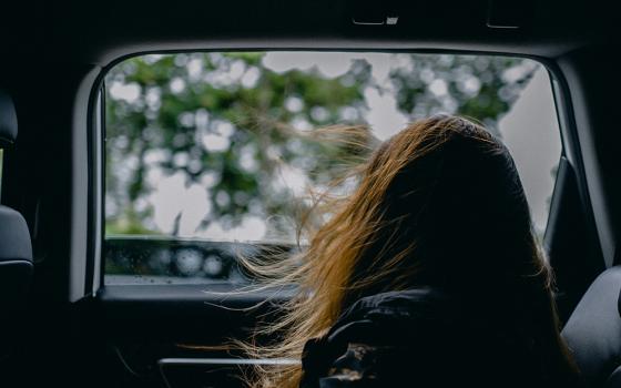 A girl looking out the window of the backseat of a car (Unsplash/Ham Kris)