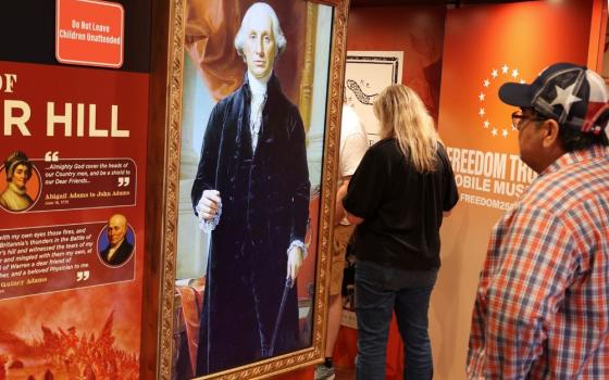 A visitor stands in front of an AI-animated image of George Washington inside the "Freedom Truck" parked at the La Crosse convention center for the "Zeale for America 250 Rally." (Martyn Smith)