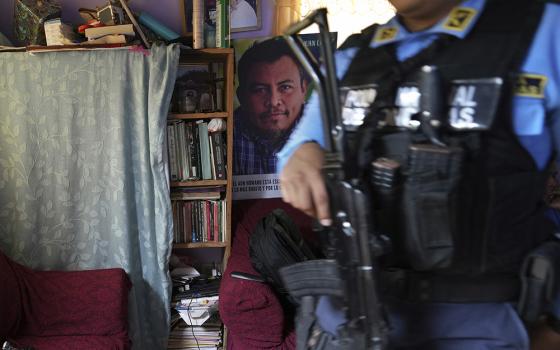 A poster of slain environmentalist Juan López hangs in his home as a state-assigned bodyguard watches over the López family, in Tocoa, Honduras, Dec. 6, 2024. (AP photo/Moises Castillo)