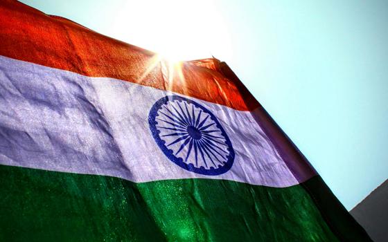 The Indian flag is backlit by the sun, with a blue sky in the background, in a close-up, outdoor photograph. (Unsplash/Aniyora J)